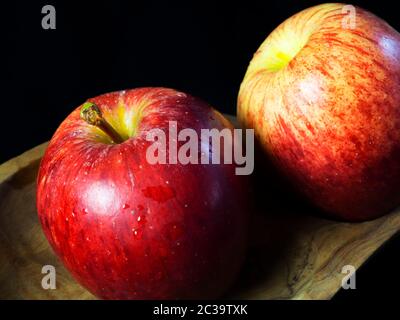 Deux pommes braeburn lavées avec des gouttelettes d'eau dans un plat en bois sur fond noir Banque D'Images