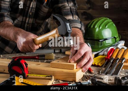 Close-up. Carpenter avec marteau, clous fixe une planche de bois. L'industrie de la construction, faire vous-même. Table de travail en bois. Banque D'Images