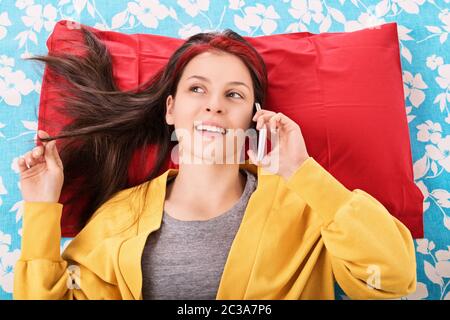 Communication, amitié concept. Belle jeune femme au lit, jouant avec ses cheveux et parlant sur le téléphone portable. Jeune fille au lit smilin Banque D'Images