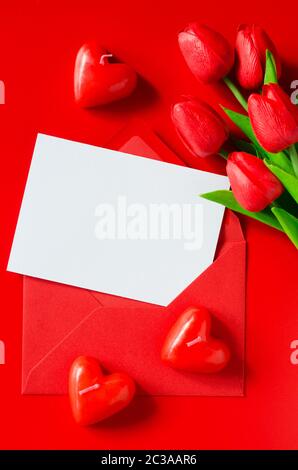 Carte de souhaits pour la Saint-Valentin, la Journée de la femme ou la Fête des Mères. Enveloppe rouge avec du papier blanc, bouquet de tulipes et de bougies en forme de coeur. Vue supérieure de la wi Banque D'Images