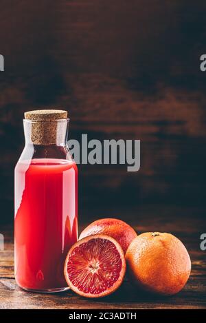 Bouteille de jus d'orange sanguine avec des fruits coupés en deux sur la table en bois Banque D'Images