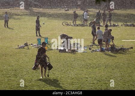 Après un après-midi de soleil et de températures chaudes pendant le maintien du coronavirus britannique, une pluie soudaine et torrentielle attire les utilisateurs du parc par surprise, à Ruskin Park, un espace vert public à Lambeth, le 14 juin 2020, à Londres, en Angleterre. Le nombre actuel de décès de Covid-19 au Royaume-Uni s'élève désormais à 41,662, soit une augmentation par rapport aux 24 dernières heures de 181, Bien que le Premier ministre Boris Johnson soit sous pression pour examiner les arguments en faveur d’une réduction de la règle de la distance sociale de 2 mètres, en raison de son effet sur l’emploi et l’économie en général. Banque D'Images