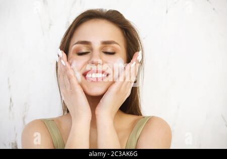 Belle jeune femme caucasienne lavant son visage avec de la mousse Banque D'Images