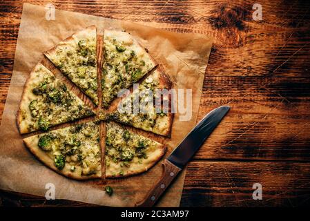 Tranches de pizza italienne avec brocoli, sauce pesto, épices et fromage sur du papier sulfurisé sur table en bois rustique. Vue de dessus Banque D'Images