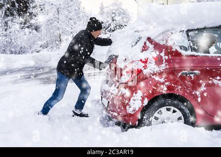 Homme poussant une voiture prise dans la neige après les fortes chutes de neige Banque D'Images