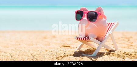 Pink Piggybank portant des lunettes sur une chaise longue sur la plage de sable Banque D'Images