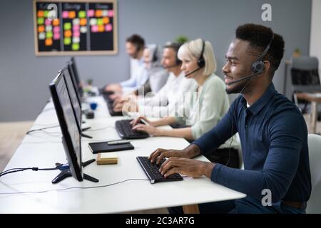 L'agent des services à la clientèle masculine positive avec casque de travail dans un centre d'appels Banque D'Images