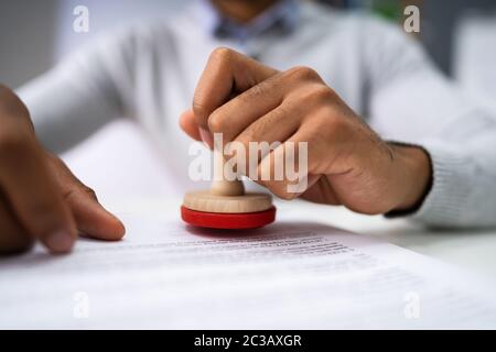 Close-up of a person's Hand Stamping avec timbre approuvé sur le document At Desk Banque D'Images