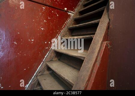 Vieux escaliers en bois brun endommagé et mur rouge menant au grenier, a besoin de rénovation près Banque D'Images