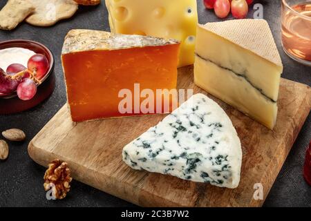 Plaque à fromage. Fromage bleu, Leicester rouge, fromage de chèvre et Emmental, sur une assiette en bois avec du raisin Banque D'Images