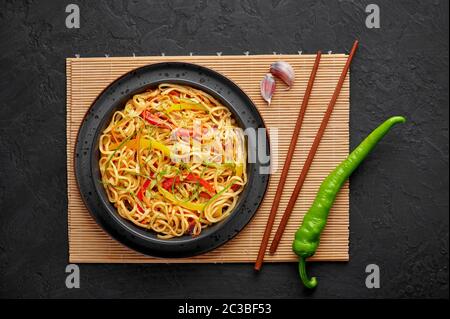 Nouilles Hakka à l'ail de piment dans un bol noir sur un dessus en tabpe d'ardoise sombre. Indo-chinois plat végétarien. Nouilles à légumes indiennes. Classique A. Banque D'Images