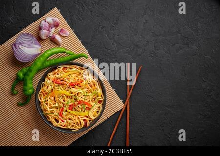 Nouilles Hakka à l'ail de piment dans un bol noir sur un dessus en tabpe d'ardoise sombre. Indo-chinois plat végétarien. Nouilles à légumes indiennes. Classique A. Banque D'Images