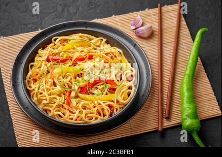 Nouilles Hakka à l'ail de piment dans un bol noir sur un dessus en tabpe d'ardoise sombre. Indo-chinois plat végétarien. Nouilles à légumes indiennes. Classique A. Banque D'Images