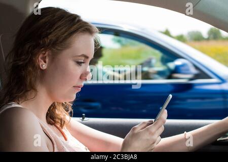 Une jeune femme conduit une voiture et écrit un message sms Banque D'Images