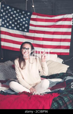 Jolie femme en tenue décontractée sur le lit avec drapeau américain sur le mur Banque D'Images