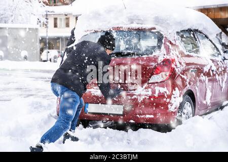 Homme poussant une voiture prise dans la neige après les fortes chutes de neige Banque D'Images