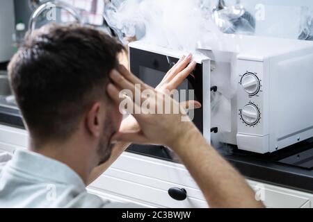 Jeune homme pulvérisant extincteur sur le four à micro-ondes dans la cuisine Banque D'Images