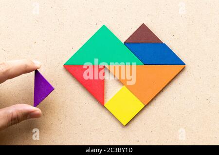 Puzzle couleur en forme de coeur qui attend la pièce triangulaire pour remplir la forme sur fond de bois Banque D'Images
