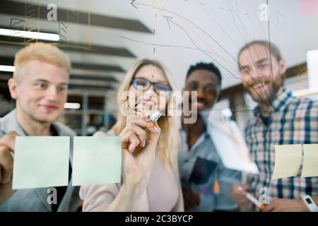 Concept d'entreprise, de démarrage, de planification et de personnel. Jolie femme blonde en lunettes dessin schéma de tableau sur panneau de verre avec des autocollants pour la création Banque D'Images