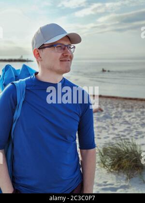 Portrait d'un jeune homme beau debout avec un panneau SUP sur une plage de sable blanc en mer Baltique Banque D'Images