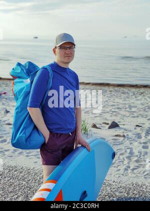 Portrait d'un jeune homme beau debout avec un panneau SUP sur une plage de sable blanc en mer Baltique Banque D'Images