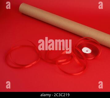 Rouleau de papier brun d'emballage, d'une bobine de ruban rouge et un cadeau enveloppé dans du papier kraft brun sur un fond rouge, faisant de surprises Banque D'Images