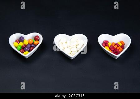 Soucoupe en forme de coeur rempli de bonbons colorés sur fond noir. Illustration de la Saint-Valentin. Top vues Banque D'Images