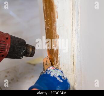 Détail de la suppression de la peinture blanche ancienne du cadre de porte avec pistolet thermique et racleur Banque D'Images