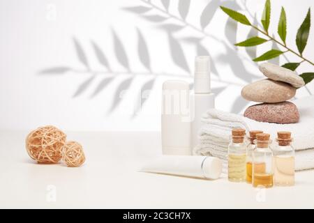 Spa still life with creams, essential oils, stones and towels on light background with shadow from plant. Healthy lifestyle, body care, Spa treatment. Banque D'Images