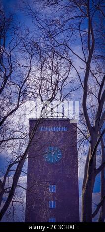 Tour d'horloge en brique rouge contre ciel bleu clair et nuages blancs, vu à travers les branches d'arbres. Tour de l'horloge de la gare centrale d'Oberhausen, Ger Banque D'Images