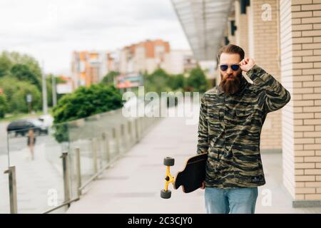 Jeune homme marchant avec la longboard dans la rue Banque D'Images