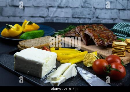 Côtes sous sauce au miel sur une planche en bois à côté de tomates, poivrons et basilic au romarin, feta tranché avec cracker. Vues de dessus Banque D'Images