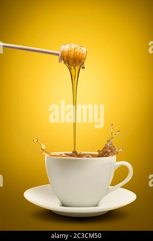 Le miel s'écoule dans une tasse de thé, sur fond jaune Banque D'Images