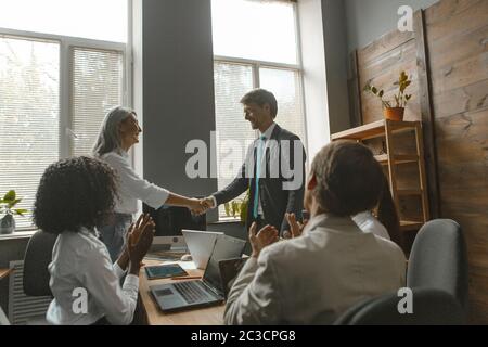 Les gens d'affaires se secouent la main. Le chef de projet se met la main avec l'employé pour applaudir l'équipe assise à la table de négociation au bureau. Image en tons Banque D'Images