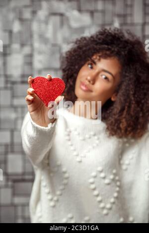 Un coeur rouge de papier dans les mains d'une jeune fille africaine à poil frisé. Se concentrer sur le coeur, peu profonde profondeur de foyer Banque D'Images