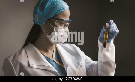 Médecin regardant sur une sonde de test avec du sang de Covid 19 coronavirus infecté. Un professionnel médical de laboratoire sérieux l'examine en préparation pour les tests de vaccins. Gros plan Banque D'Images