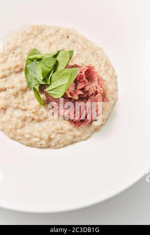 Vue rapprochée du porridge de flocons d'avoine avec du jambon à faible teneur en matières grasses et des épinards frais. Banque D'Images