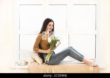 Bonne femme avec des fleurs assis sur le rebord de la fenêtre Banque D'Images