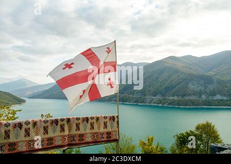 Drapeau de Géorgie sur un fond de paysage de montagne et de lac Banque D'Images