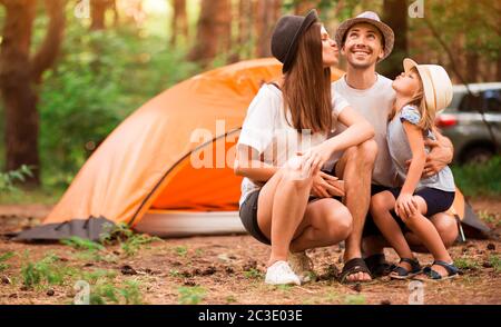 Portrait de beaux jeunes parents et de leur petite fille mignonne qui s'embrasse, regardant l'appareil photo et souriant. Les filles embrassaient leur père tout en se reposer à l'extérieur Banque D'Images