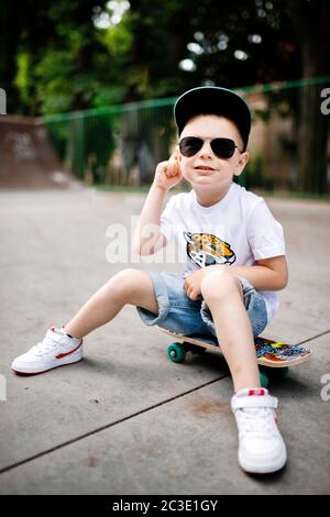 Garçon avec un skate dans un parc de skate. Le garçon est assis sur un skateboard dans une tenue élégante. Un peu extrême Banque D'Images