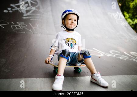 Garçon avec un skate dans un parc de skate. Le garçon apprend à skate, en pleine protection. Banque D'Images