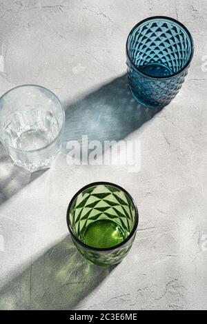 Trois verres de verre géométrique dans les couleurs bleu, vert et transparent avec des rayons de lumière d'ombre colorés sur fond de béton de pierre, angle de vue élevé Banque D'Images