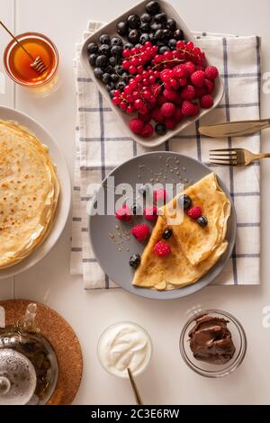 Disposition plate de la table de cuisine servi pour le petit déjeuner avec baies fraîches, crêpes appétissantes, crème à la crème, miel et tartiner au chocolat Banque D'Images