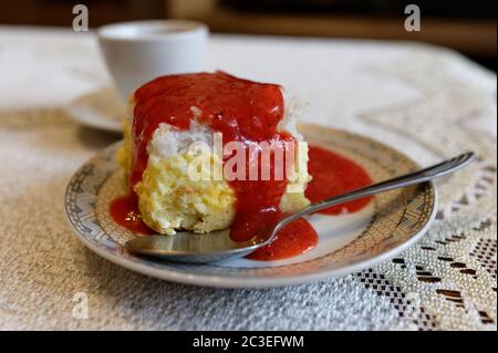 Morceau de gâteau au fromage avec garniture fraise sur une assiette avec une cuillère, sur une nappe blanche avec une tasse en arrière-plan Banque D'Images