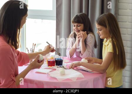 la mère et deux filles à la table peignent des œufs de pâques Banque D'Images