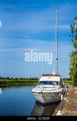 Bateau à moteur ou bateau à voile blanc ancré sur le quai du lac ou quai avec roseaux et essais de rivière verte Banque D'Images