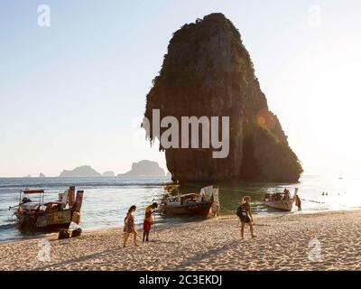 Krabi, Thaïlande - 14 février 2019 : plage de Phra nang, marché flottant. Bateaux de restauration. Vente de fast-food et de boissons à bord des bateaux, Menu à la poupe du navire. L'homme nettoie la plage des ordures. Les touristes se promène près de lui. Banque D'Images