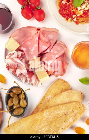 Cuisine italienne. Jambons et fromages, pain, câpres et vin, tiré d'en haut sur un fond blanc Banque D'Images