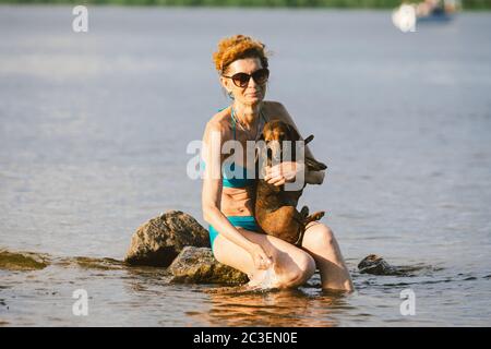 Femme adulte Profitez de la journée à la plage avec un chien. La propriétaire, femme en maillot de bain et petit chien de dachshund brun, passe leur temps d'été à se rafraîchir dans le froid Banque D'Images